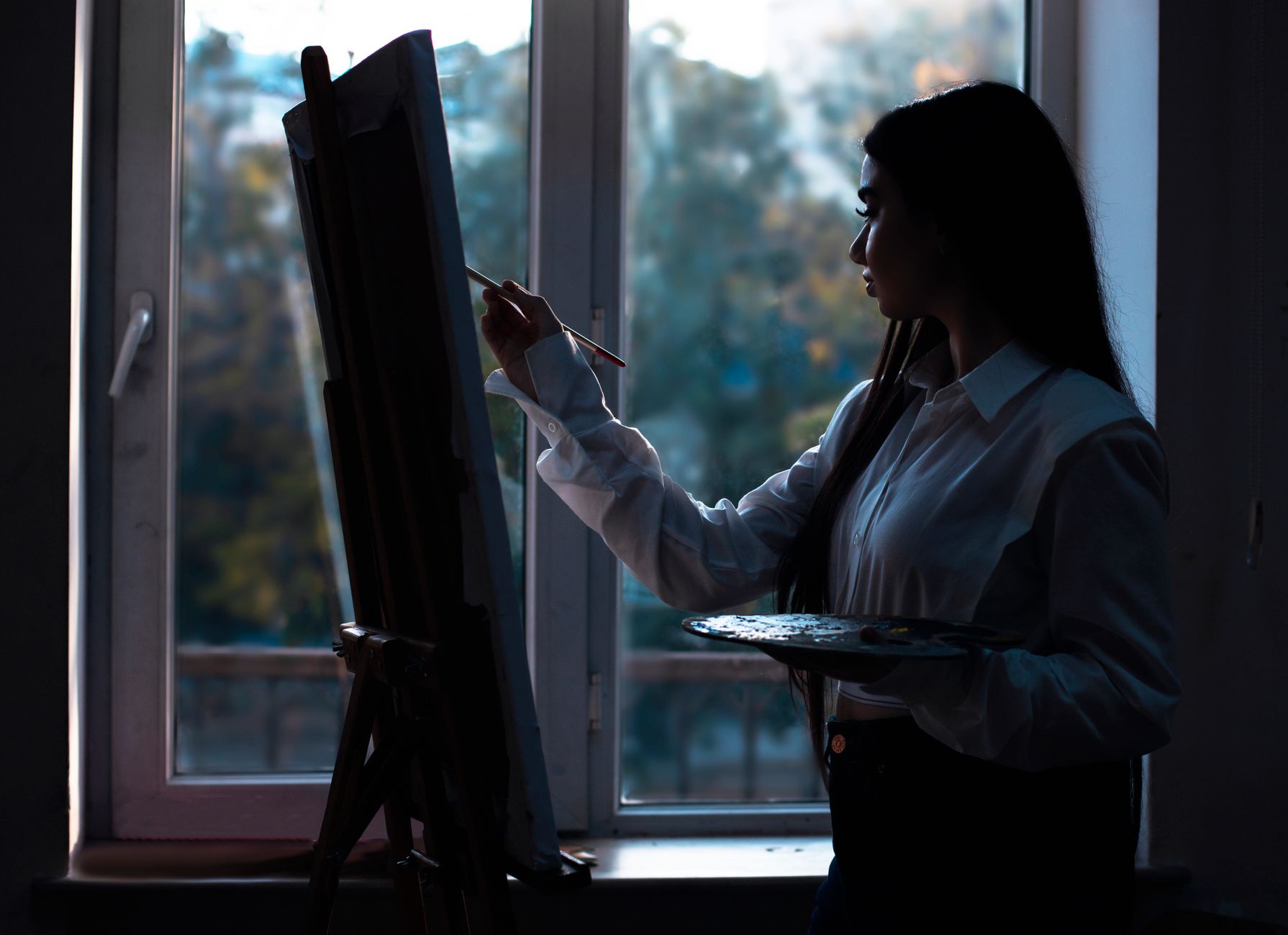 An artist silhouetted while working by a window at twilight