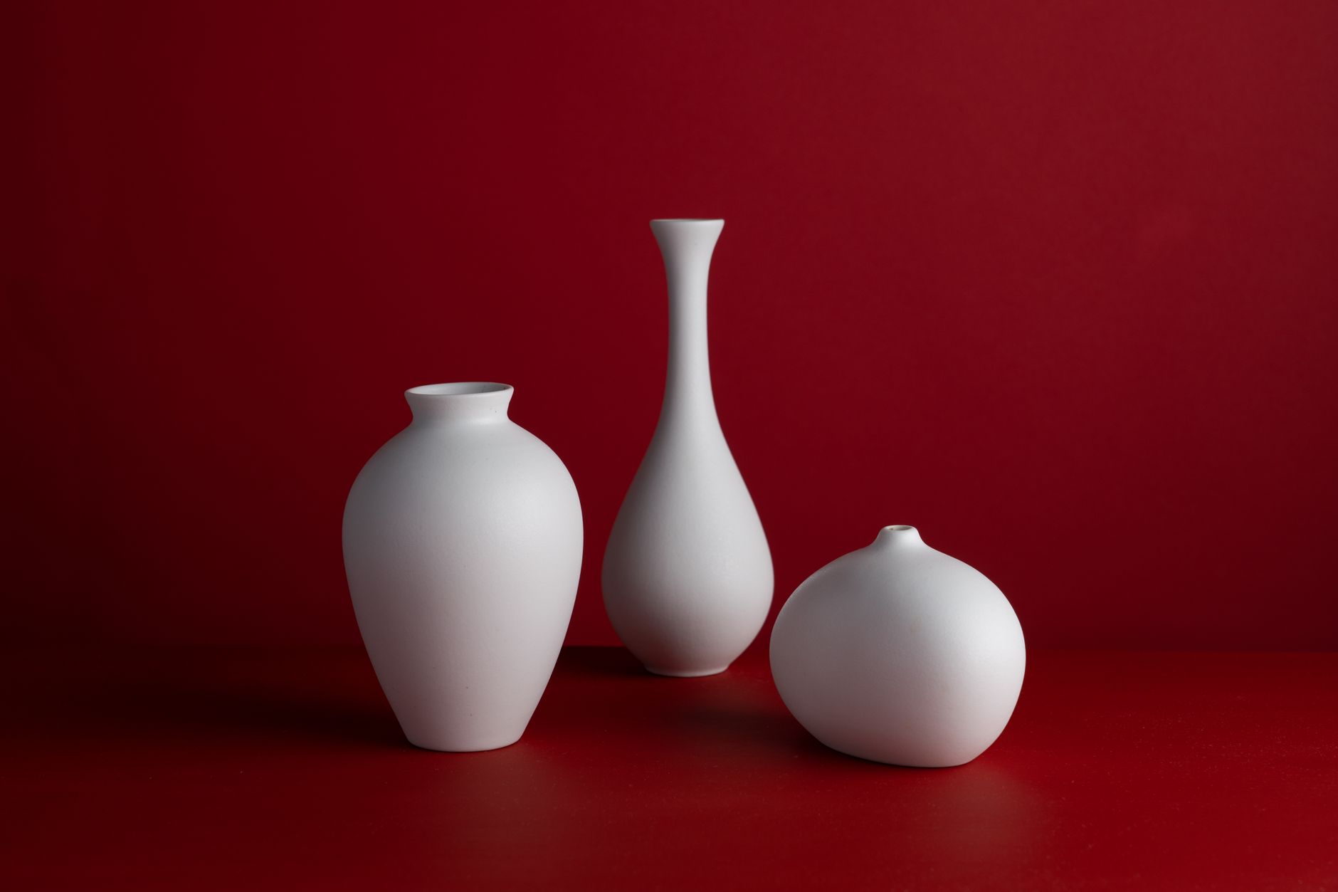Three white ceramic vases against a red background